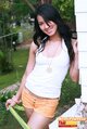 Leaning against wall wearing white top in orange shorts